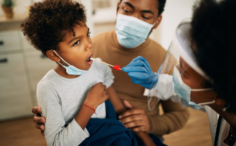 African American boy sitting in father's lap while going through PCR testing at home due to COVID-19 pandemic.